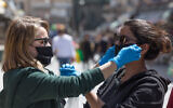 Women help each other to put on face masks at Jerusalem's Mahane Yehuda fruit and vegetable market, April 3, 2020 (Nati Shohat/Flash90)