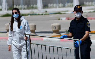 Police and Magen David Adom personnel at a drop off station for residents from the ultra Orthodox city of Bnei Brak who have been infected by the coronavirus, and are on their way to quarantine hotels, near Rama Gan's Ayalon mall on April 3, 2020 (Tomer Neuberg/ Flash90)