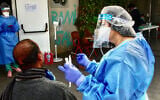 Medical workers wearing full protective clothing at a site to collect samples for coronavirus testing in south Tel Aviv on April 6, 2020. (Avshalom Sassoni/Flash90)