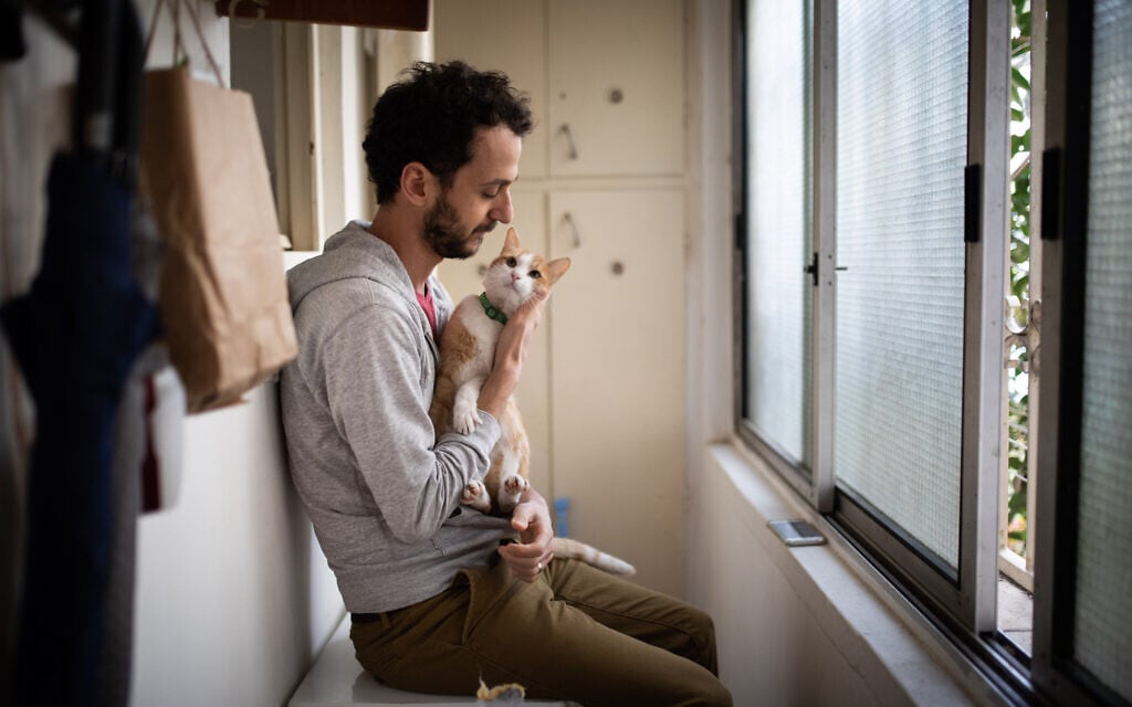 A man pets his cat as he sits by the window of his apartment during a nationwide quarantine, in Jerusalem, on March 18, 2020. (Hadas Parush/Flash90) A man pets his cat as he sits by the window of his apartment during a nationwide quarantine, in Jerusalem, on March 18, 2020. (Hadas Parush/Flash90)