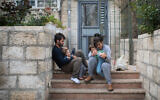 An Israeli family sits on the steps outside their apartment building in Jerusalem, as they stay at home with their children during a nation-wide quarantine, on March 31, 2020. (Hadas Parush/Flash90)