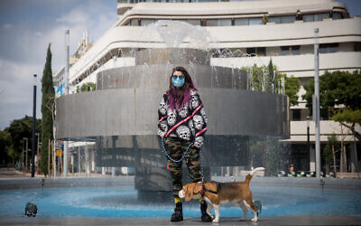 A woman wearing a protective face mask with her dog in Dizengoff Square in Tel Aviv, April 11, 2020. (Miriam Alster/Flash90)
