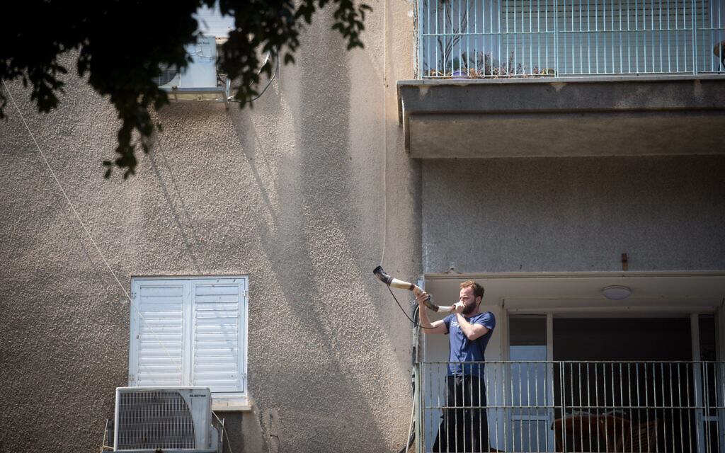 Illustrative: A man blows a shofar horn from his balcony in Tel Aviv on April 14, 2020. (Miriam Alster/Flash90)