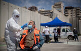 Magen David Adom medical workers seen at a drive-through site to collect samples for coronavirus testing, alongside the security barrier outside Shuafat Refugee Camp, Jerusalem, April 16, 2020. (Yonatan Sindel/Flash90)