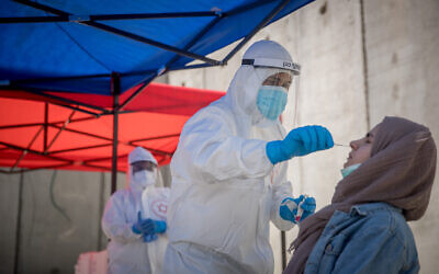 Magen David Adom medical workers seen at a drive-through site to collect samples for coronavirus testing, alongside the security barrier outside Shuafat Refugee Camp, Jerusalem, April 16, 2020. (Yonatan Sindel/Flash90)