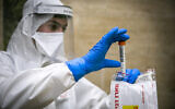 Magen David Adom medical team members, wearing protective gear, handle a coronavirus test from patients in Jerusalem, April 17, 2020. (Olivier Fitoussi/Flash90)