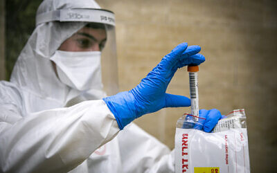 Magen David Adom medical team members, wearing protective gear, handle a coronavirus test from patients in Jerusalem, April 17, 2020. (Olivier Fitoussi/Flash90)