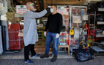 A worker checks the temperature of a customer at a store in the northern Arab Israeli town of Deir al-Asad on April 18, 2020. (Basel Awidat/Flash90)
