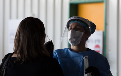 A Shaare Zedek Medical team member wearing protective gear takes a swab from a woman to test for the coronavirus disease (COVID-19), outside the coronavirus unit at Shaare Zedek hospital in Jerusalem on April 20, 2020. (Nati Shohat/Flash90)