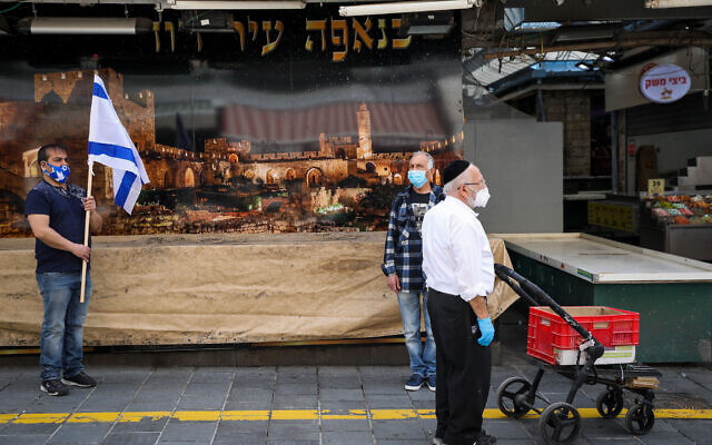 People stand still at the Mahane Yehuda Market in Jerusalem, as a two-minute siren sounds across Israel to mark Holocaust Remembrance Day on April 21, 2020 (Olivier Fitoussi/Flash90) People stand still at the Mahane Yehuda Market in Jerusalem, as a two-minute siren sounds across Israel to mark Holocaust Remembrance Day on April 21, 2020 (Olivier Fitoussi/Flash90)