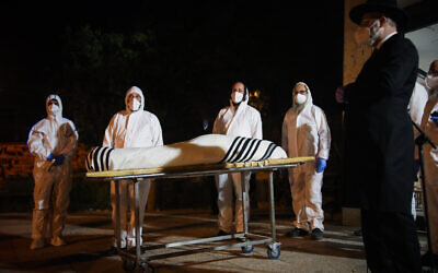 Chevra Kadisha workers wearing protective clothes, carry the body of Rabbi Avraham Heber who died from complications of the Coronavirus (COVID-19) infection, at the Shamgar Funeral Home in Jerusalem, on April 23, 2020. (Yonatan Sindel/Flash90)