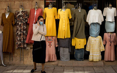 A woman wearing a protective face mask walks past a clothes shop in Jerusalem on April 26, 2020. (Nati Shohat/Flash90)