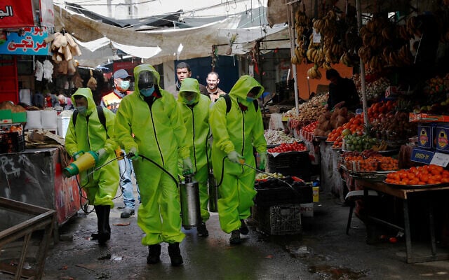 Workers wearing protective gear spray disinfectant as a precaution against the coronavirus at the main market in Gaza City, March 27, 2020. (AP/Adel Hana) Workers wearing protective gear spray disinfectant as a precaution against the coronavirus at the main market in Gaza City, March 27, 2020. (AP/Adel Hana)