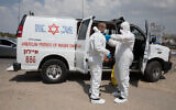 Magen David Adom workers wearing protective clothing disinfect their ambulance after taking care of a patient with a possible coronavirus infection on April 14, 2020 (Nati Shohat/Flash90)