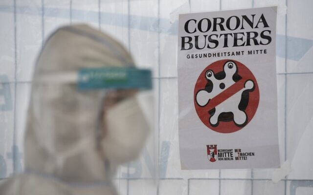 A health professional wearing protective gear, face shield and face mask stands next to a "Corona Busters" poster hanging at a drive-in COVID-19 testing facility in Berlin on April 30, 2020, amid the new coronavirus COVID-19 pandemic. (John MACDOUGALL / AFP) A health professional wearing protective gear, face shield and face mask stands next to a "Corona Busters" poster hanging at a drive-in COVID-19 testing facility in Berlin on April 30, 2020, amid the new coronavirus COVID-19 pandemic. (John MACDOUGALL / AFP)