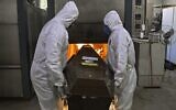 Crematorium workers wearing personal protective equipment as a preventive measure against the spread of the coronavirus pandemic, push a corpse into the oven of its crematorium at Sao Francisco Xavier cemetery, in Rio de Janeiro, Brazil on May 29, 2020 (CARL DE SOUZA / AFP)