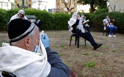 Illustrative: Religious Jewish men pray while keeping a distance from each other outside their closed synagogue in Netanya on April 23, 2020. (Jack Guez/AFP)