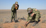 In this May 5, 2020 frame from video, Alfred Abayev, head of a volunteer group searching for remains of the WW II Red Army soldiers, right, looks at projectile left on a WW II battlefield near Khulkhuta in the province of Kalmykia in southern Russia. The search is part of a broad effort by myriad volunteer groups across the country to pay tributes to the fallen WW II soldiers. (AP Photo/Radik Nurmukhamedov)