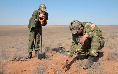 In this May 5, 2020 frame from video, Alfred Abayev, head of a volunteer group searching for remains of the WW II Red Army soldiers, right, looks at projectile left on a WW II battlefield near Khulkhuta in the province of Kalmykia in southern Russia. The search is part of a broad effort by myriad volunteer groups across the country to pay tributes to the fallen WW II soldiers. (AP Photo/Radik Nurmukhamedov)