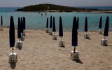 Rows of closed parasols on a nearly empty stretch of Nissi beach with a few beachgoers in the distance in Cyprus seaside resort of Ayia Napa, May 13 2020. (Petros Karadjias/AP)