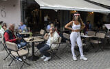 A cafe-restaurant worker stands outside as people drink coffee in Monastiraki district of Athens, May 25, 2020. (AP Photo/Petros Giannakouris)