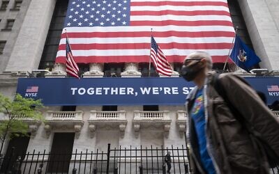 A man wearing a protective face mask passes the New York Stock Exchange, Tuesday, May 26, 2020, as employees arrive for the partial reopening of the trading floor. (AP Photo/Mark Lennihan)