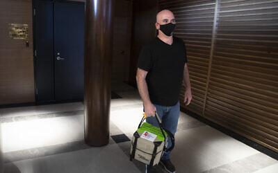 In this May 19, 2020, photo, Israeli courier, Mishel Zrian carries a bone marrow transplant donation at Ben Gurion airport near Tel Aviv, Israel. Over the past two months, as air travel has ground to a halt, Zrian has criss-crossed the Atlantic and the United States dozens of times, sleeping in empty airports and unable to return home to see his family in Israel, all in a race against time to deliver life-saving transplants. (AP Photo/Sebastian Scheiner)