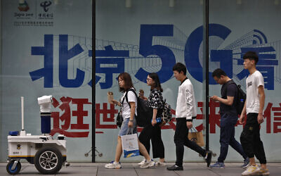 Illustrative: A police robot mounted with surveillance cameras watches people walking past a 5G network advertisement in a shopping district in Beijing, Wednesday, May 15, 2019. (AP/Andy Wong)