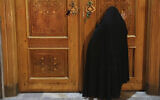 A woman prays behind a closed door of Masoume shrine in the city of Qom, some 80 miles (125 kilometers) south of the capital Tehran, Iran, March 16, 2020 (AP Photo/Str)