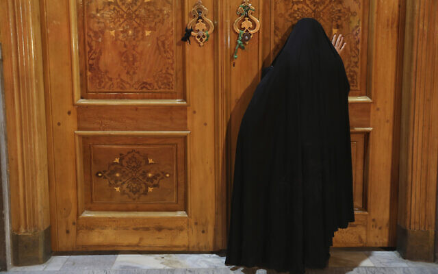 A woman prays behind a closed door of Masoume shrine in the city of Qom, some 80 miles (125 kilometers) south of the capital Tehran, Iran, March 16, 2020 (AP Photo/Str)