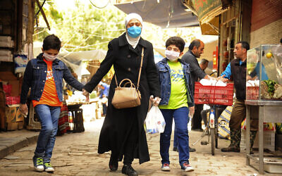 In this photo released on April 18, 2020, a Syrian woman walks with her sons wearing masks due to the coronavirus, in Damascus, Syria. (SANA via AP)