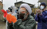 Mourners wearing protective clothing, face masks and gloves, pray over the body of a victim who died after being infected with the new coronavirus, in the outskirts of the Iranian city of Babol on April 30, 2020. (AP Photo/Ebrahim Noroozi)