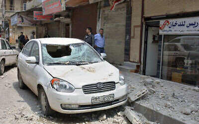 Illustrative: People stand near a car that was damaged due to flying debris from a Syrian military base housing a weapons warehouse, in the country's central province of Homs, Syria, May 1, 2020. (SANA, the Syrian official news agency, via AP)