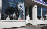 Broken glass and a stone lie on the pavement as an Israeli flag sticks out of the window of HaCarmel kosher restaurant in Amsterdam, Netherlands, May 8, 2020, after a man smashed the window (AP Photo/Peter Dejong)
