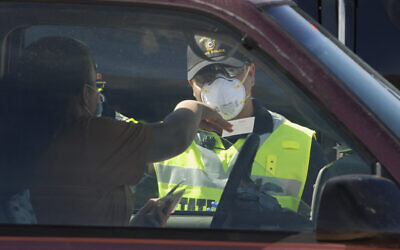 A New Mexico state police officer screens cars for compliance with an emergency lockdown order that bans nonessential visitors and limits vehicle passengers to two people as they enter Gallup, New Mexico, May 7, 2020 (AP Photo/Morgan Lee)