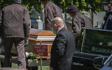Robert Salerno, center, funeral director with McLaughlin & Sons funeral home in Brooklyn, holds roses and wears a mask as cemetery workers, also wearing masks because of coronavirus restrictions, carry a casket from a hearse to a burial site on May 13, 2020, at Holy Cross Cemetery in the Brooklyn borough of New York. (AP Photo/Bebeto Matthews)