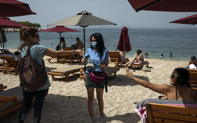 Swimmers pay for sunbeds with an employee of a beach bar who wears a protective mask against coronavirus, at Alimos beach, near Athens, on Saturday, May 16, 2020 (AP Photo/Yorgos Karahalis)