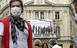 People walk backdropped by a banner showing victims executed by hanging in 1945 by the pro-Nazi Croatian WWII Ustasha regime in Sarajevo, Bosnia, on May 16, 2020. (AP/Kemal Softic)