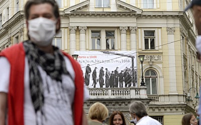 People walk backdropped by a banner showing victims executed by hanging in 1945 by the pro-Nazi Croatian WWII Ustasha regime in Sarajevo, Bosnia, on May 16, 2020. (AP/Kemal Softic)
