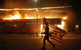 A protester carries a US flag upside down, a sign of distress, next to a burning building Thursday, May 28, 2020, in Minneapolis (AP Photo/Julio Cortez)
