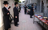 Ultra-Orthodox Jewish men pray outside a closed yeshiva in Bnei Brak on March 26, 2020. (Tomer Neuberg/Flash90)