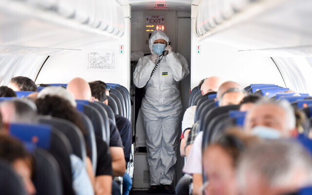 Illusrative: An Israir flight attendant wearing full protective gear walks next to passengers during an Israir flight between Tel Aviv and Eilat, May 13, 2020. (Yossi Zeliger/Flash90) Illusrative: An Israir flight attendant wearing full protective gear walks next to passengers during an Israir flight between Tel Aviv and Eilat, May 13, 2020. (Yossi Zeliger/Flash90)