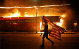 A protester carries a US flag upside down, a sign of distress, next to a burning building in Minneapolis, Minnesota following the death of George Floyd, May 28, 2020. (AP/Julio Cortez)