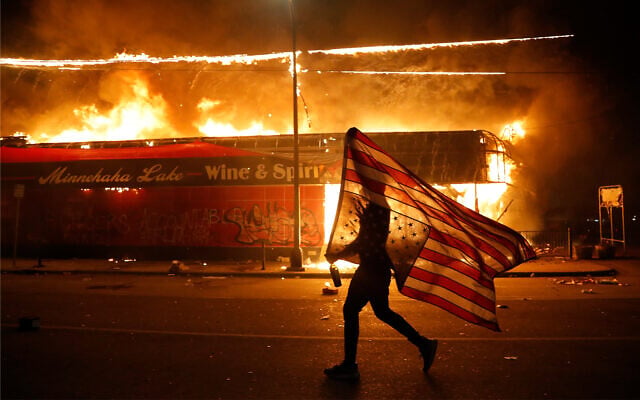 A protester carries a US flag upside down, a sign of distress, next to a burning building in Minneapolis, Minnesota following the death of George Floyd, May 28, 2020. (AP/Julio Cortez) A protester carries a US flag upside down, a sign of distress, next to a burning building in Minneapolis, Minnesota following the death of George Floyd, May 28, 2020. (AP/Julio Cortez)