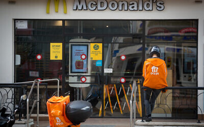 A food delivery man waits outside a McDonald's restaurant in Tel Aviv. April 18, 2020. (Miriam Alster/FLASH90)
תן ביס