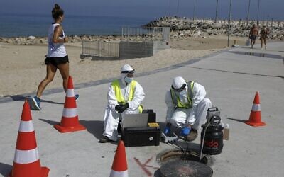 Technicians from Israeli firm Kando extract sewage samples from a manhole near the beach, in the southern coastal city of Ashkelon, on June 11, 2020. (MENAHEM KAHANA/AFP)