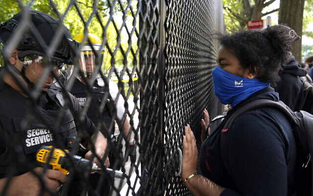 A demonstrator watches as a US Secret Service police office works on a fence blocking Lafayette Park as protests in the death of George Floyd continue, Tuesday, June 2, 2020, near the White House in Washington. Floyd died after being restrained by Minneapolis police officers. (AP Photo/Evan Vucci)