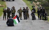 A Palestinian demonstrator holds a Palestinian flag in front of Israeli forces during a protest against US President Donald Trump's peace plan, in the Jordan Valley in the West Bank, on February 25, 2020. (AP Photo/Majdi Mohammed, File)