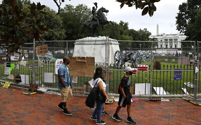 People wear face masks to protect against the spread of the new coronavirus as they walk past protest signs affixed to fencing surrounding a statue of President Andrew Jackson in Lafayette Park near the White House in Washington, June 20, 2020. (Patrick Semansky/AP)