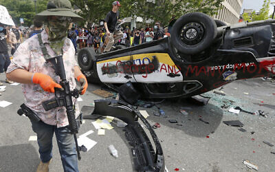 An armed protester in a Hawaiian shirt walks past a flipped over police vehicle Saturday, May 30, 2020, in Salt Lake City.  (AP/Rick Bowmer)